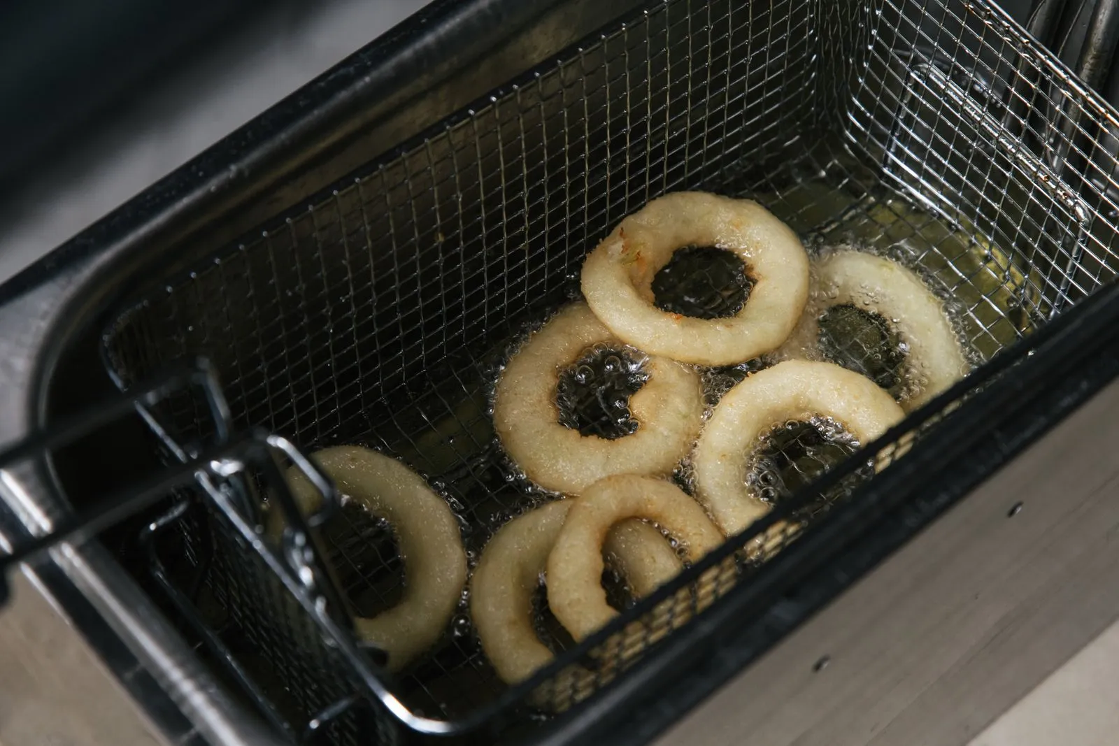 Hot crispy onion rings frying in oil in a deep fryer. Perfect food photography shot from above.